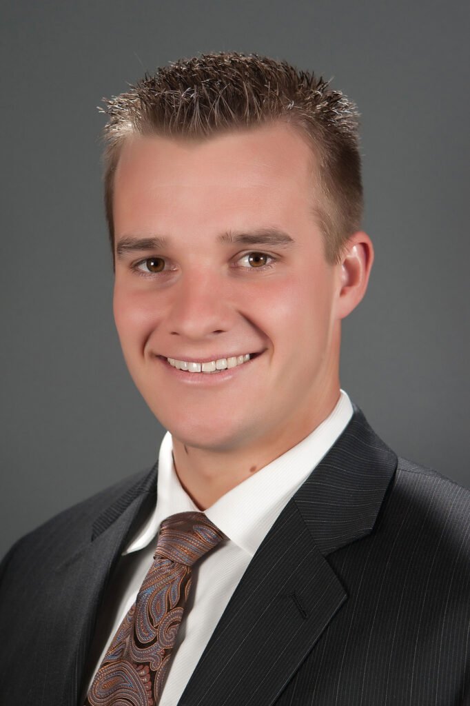 Man wearing a dark suit and patterned tie against gray