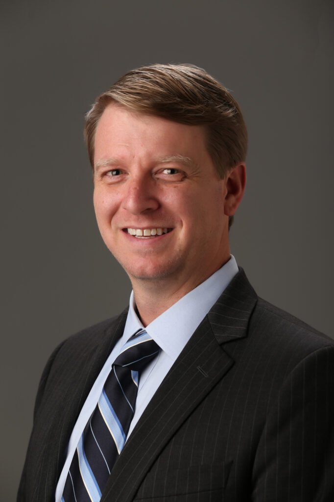 Man in a dark suit and striped tie against a gray background