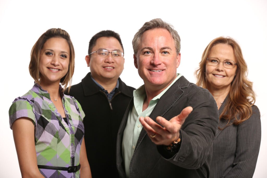 Four-person group portrait with a man gesturing toward the camera