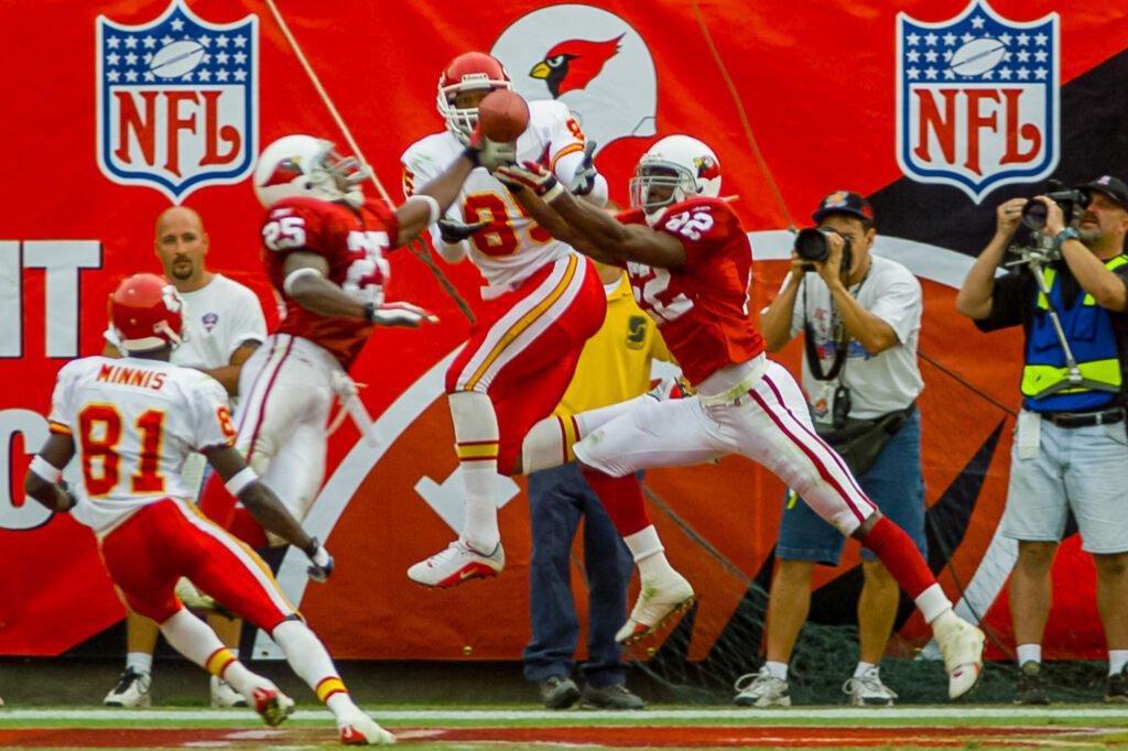 Football players leaping for a pass near sideline photographers