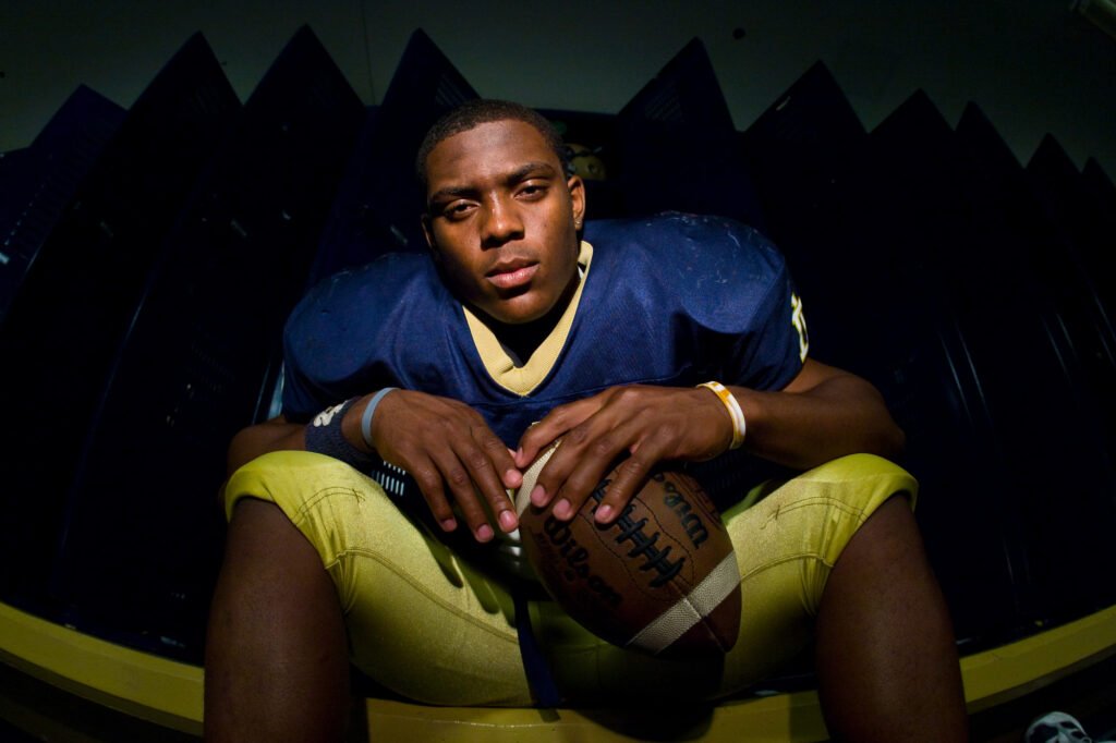 Football player seated with a ball against a dark background