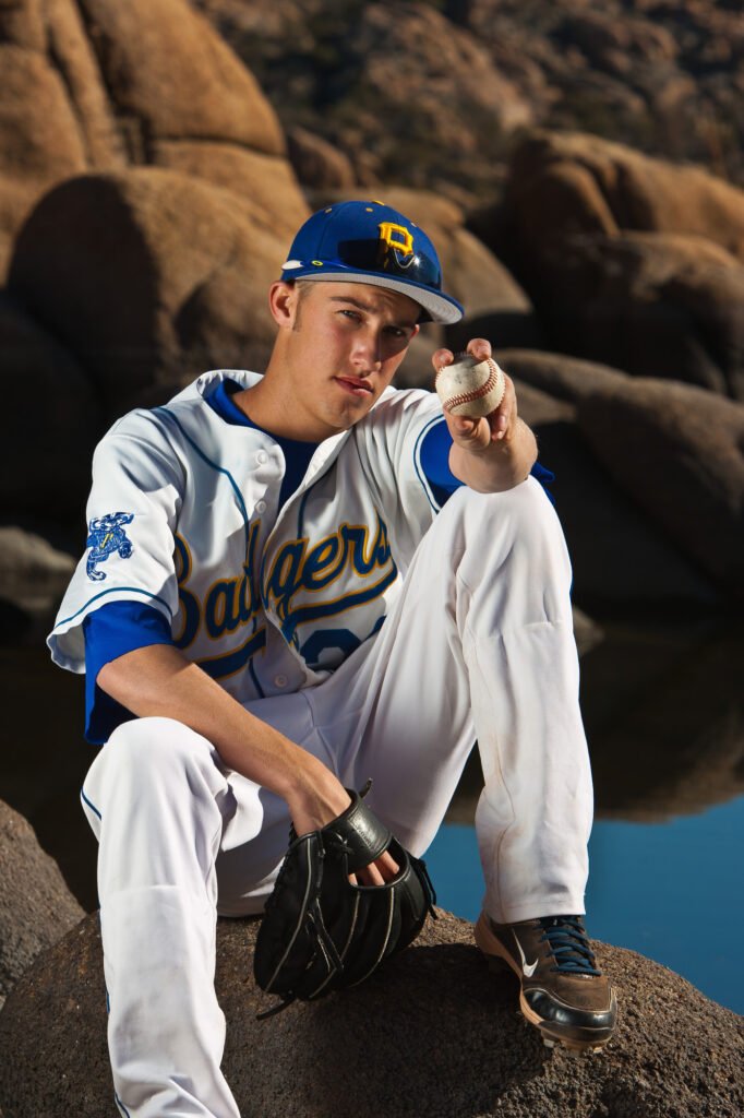 Baseball player seated on rocks and holding a ball