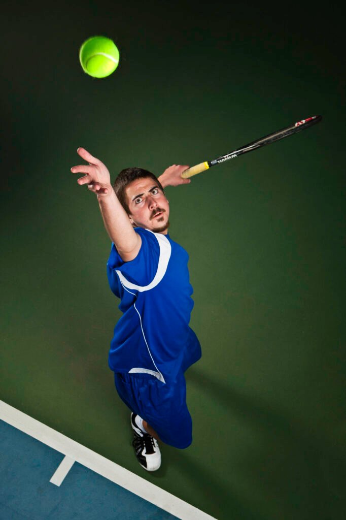 Tennis player reaching upward to serve a green ball